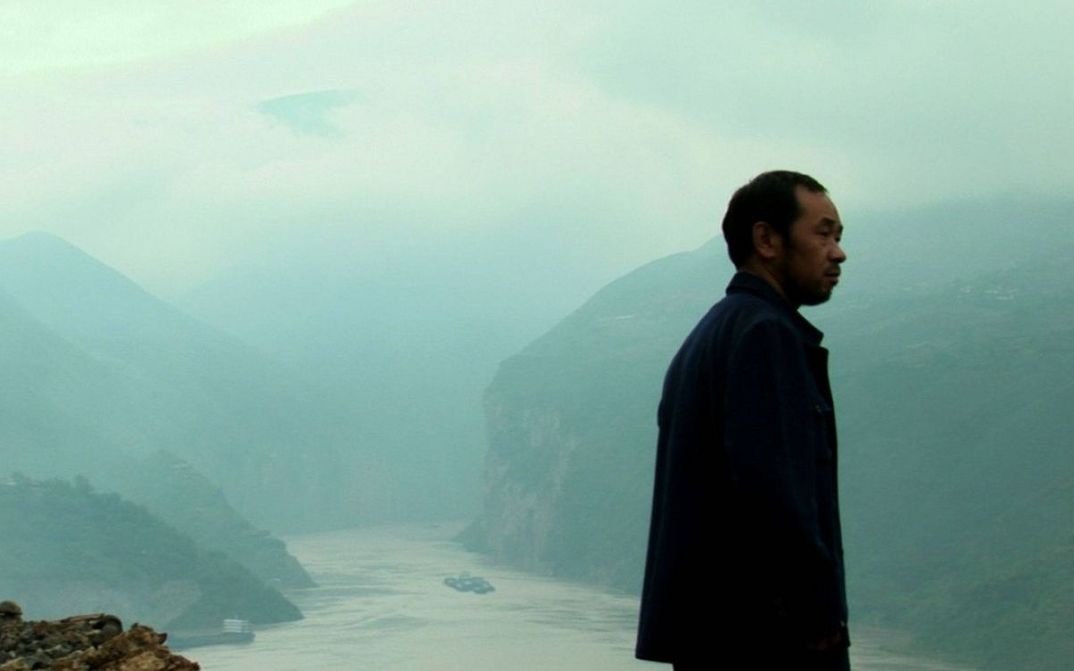 Filmstill aus STILL LIFE: Ein Mann steht erhöht und schaut nach rechts. Unter ihm ein Fluss und Berge. Es ist neblig.