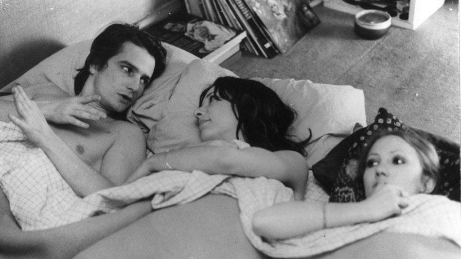 Filmstill aus LA MAMAN ET LA PUTAIN: Ein Mann und zwei Frauen liegen nebeneinander in einem Bett und unterhalten sich.