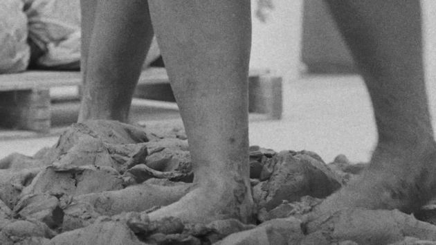 Filmstill aus dem Film „Conspiracy“ von Simone Leigh, Madeleine Hunt-Ehrlich: zwei Paar Füßen und Waden, die Lehm zerquetschen