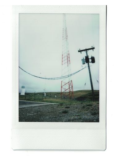 Polaroid of a radio tower and power lines, as part of a foggy landscape. 