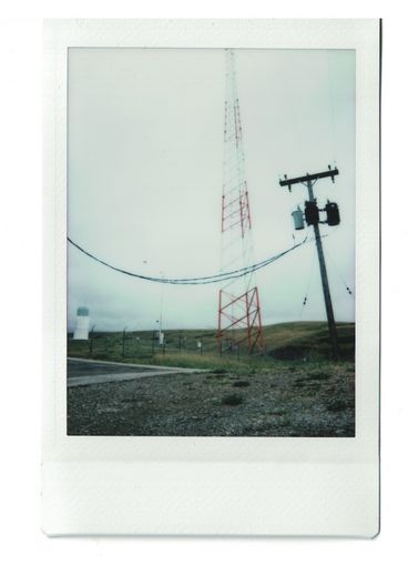 Polaroid eines Funkturms mit Stromleitungen in einer nebligen Landschaft.