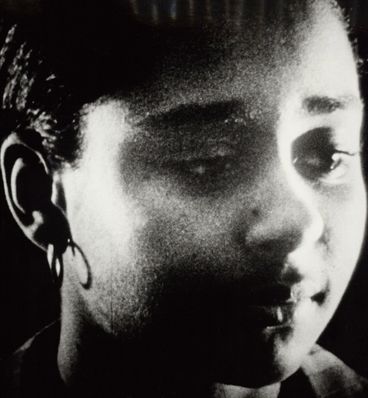 Black and white image Close-up of the face of a young woman. She is wearing creoles and glances slightly down.