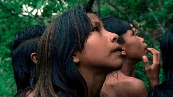 Film still from CROWRA - THE BURITI FLOWER: In the foreground, the face of a child looking upwards. Behind her, other children and the forest.