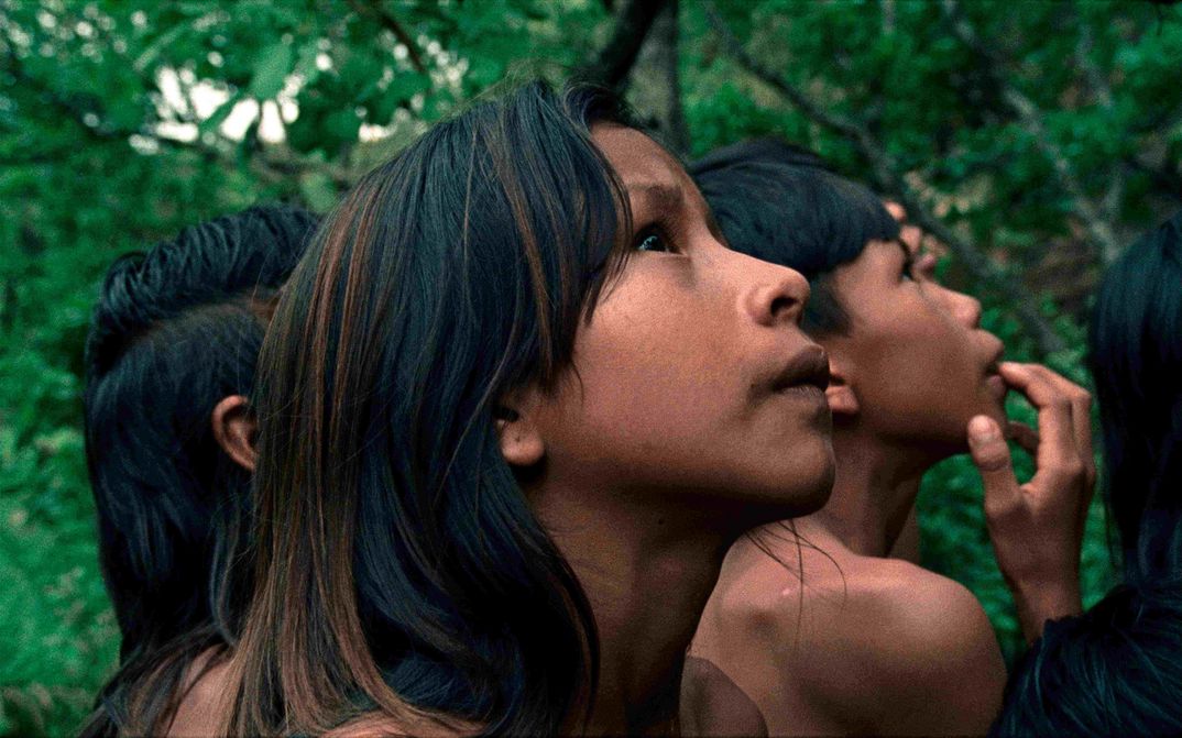 Filmstill aus CROWRA - THE BURITI FLOWER: Im Vordergrund ein Gesicht eine Kindes, das nach oben schaut. Hinter ihr weitere Kinder und Wald.