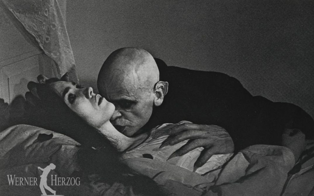Filmstill aus NOSFERATU – PHANTOM DER NACHT: Klaus Kinski als Vampir ist dabei, eine im Bett liegende junge Frau in den Hals zu beißen.