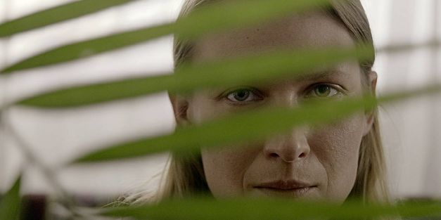 Still from the film „We Haven’t Lost Our Way“  by Anka and Wilhelm Sasnal. A woman peeks through the leaf of a plant. 
