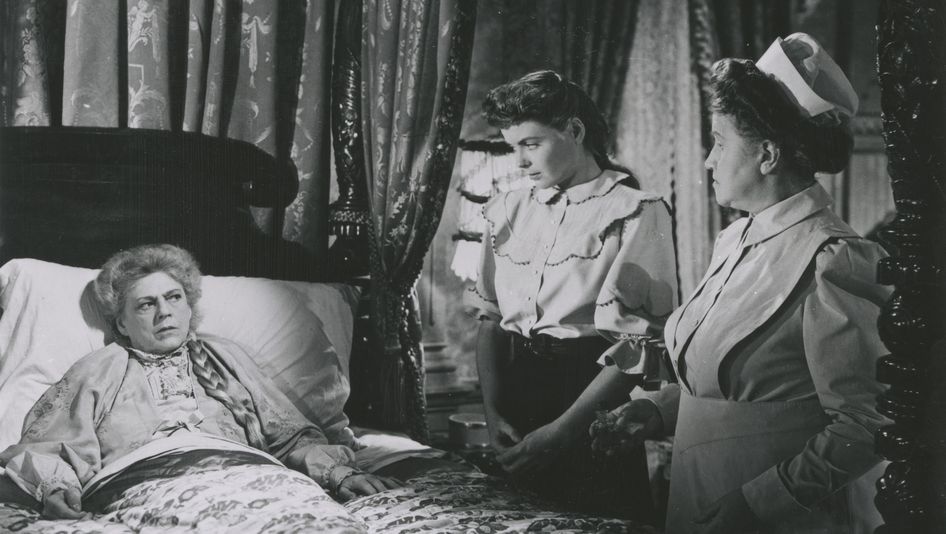 Filmstill aus THE SPIRAL STAIRCASE: Eine ältere Frau liegt im Bett, eine Krankenpflegerin und eine junge Frau stehen neben dem Bett.
