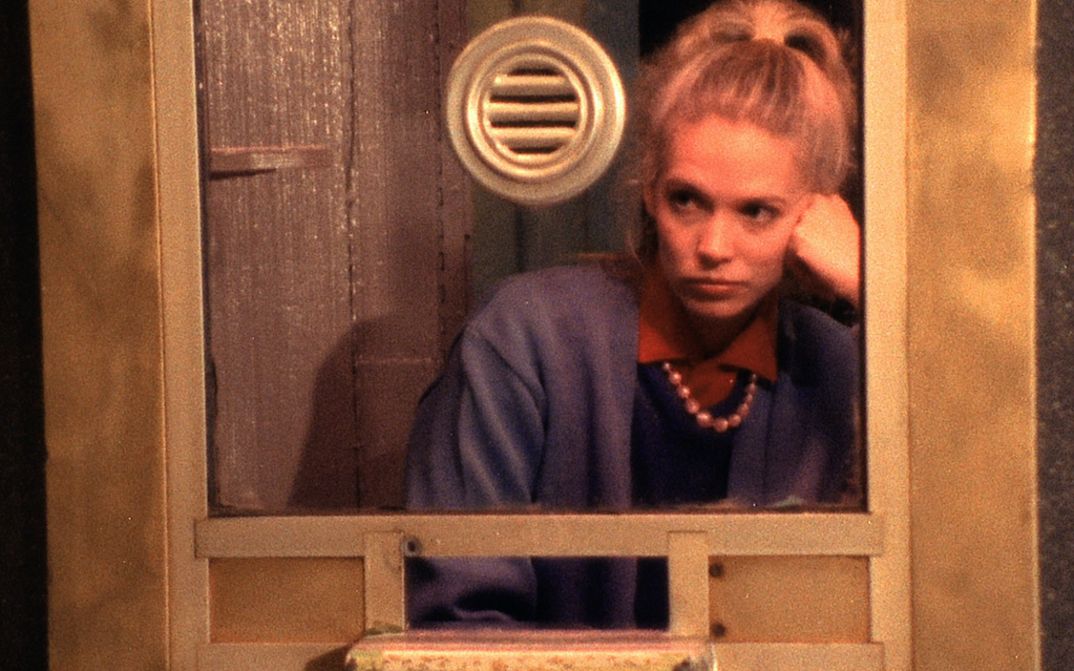 Filmstill aus VARIETY: Eine junge Frau sitzt mit gelangweiltem Gesichtsausdruck in einem Kassenhäuschen.