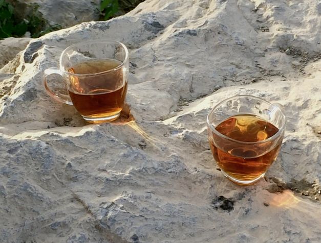 Film still from "Was hast du gestern geträumt, Parajanov?" by Faraz Fesharaki. It shows two glass cups filled with tea on a rock, illuminated by the sun. 