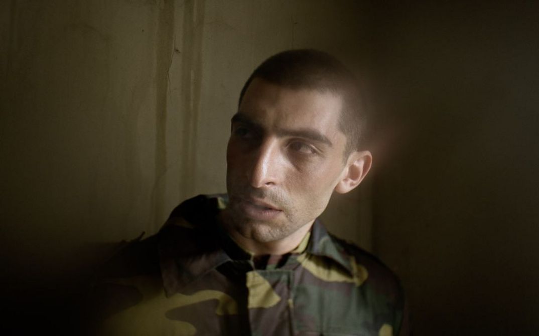 Filmstill aus AFTER DREAMING von Christine Haroutounian. Nahaufnahme eines Soldaten in Uniform vor einer Wand.