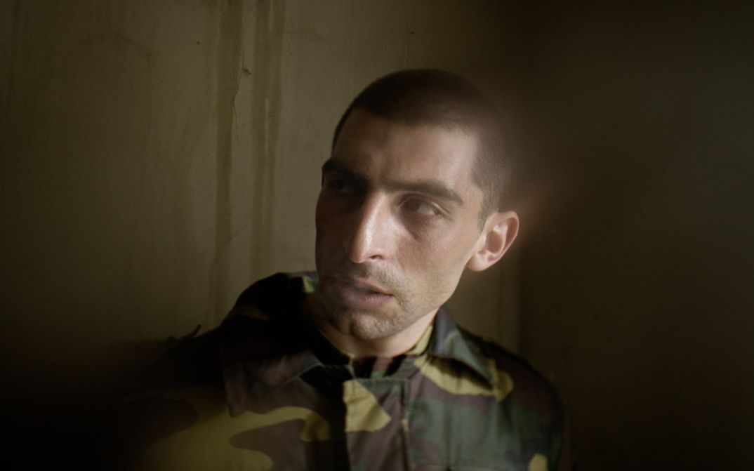 Film still from AFTER DREAMING by Christine Christine Haroutounian. Close-up of a soldier in uniform in front of a wall.