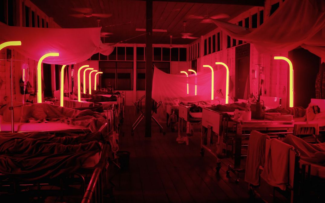 Film still from CEMETERY OF SPLENDOUR: A hospital room bathed in red light with many beds.