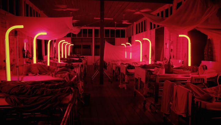 Film still from CEMETERY OF SPLENDOUR: A hospital room bathed in red light with many beds.