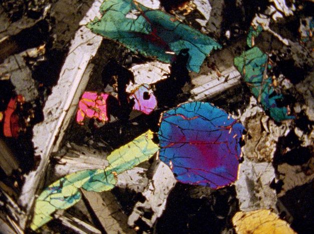 Filmstill aus „Last Things“ von Deborah Stratman. Eine Nahaufnahme oder ein Blick durch ein Mikroskop zeigt bunte, kristallähnliche Flächen..