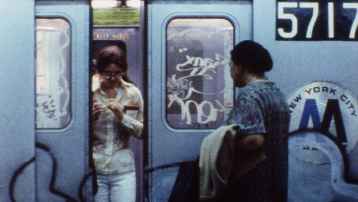 Filmstill aus NEWS FROM HOME: Die mit Graffiti bemalten Türen einer New Yorker U-Bahn öffnen sich, eine Frau steigt aus, eine andere ein. 
