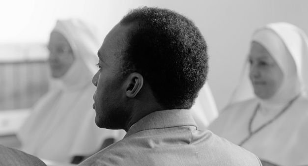 Film still from "Chroniques fidèles survenues au siècle dernier à l’hôpital psychiatrique Blida-Joinville, au temps où le Docteur Frantz Fanon était chef de la cinquième division entre 1953 et 1956" by Abdenour Zahzah. It shows a black and white close-up of the back of a person