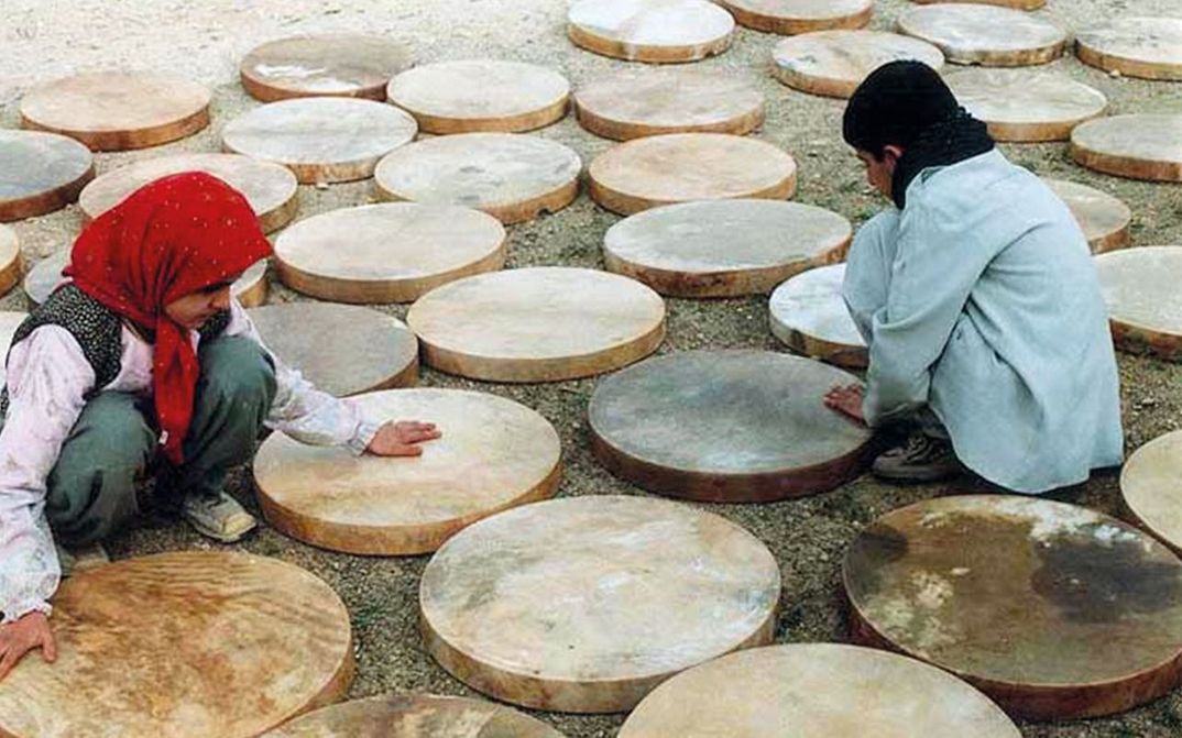 Film still from DAF: Two children crouch on the floor between half-finished drums.