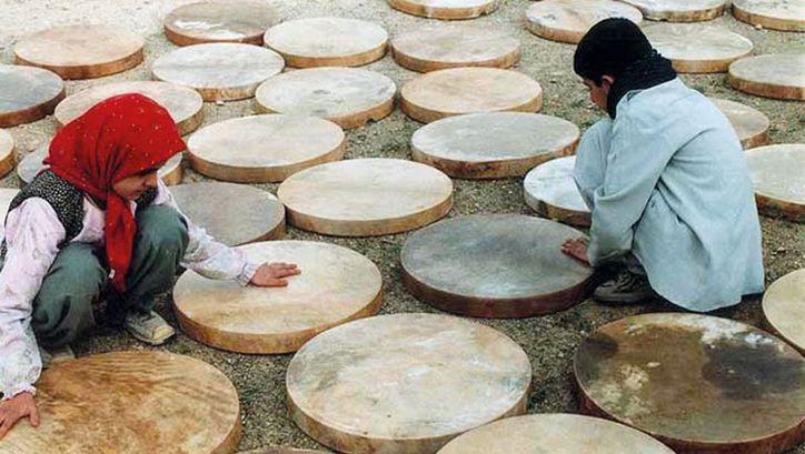Film still from DAF: Two children crouch on the floor between half-finished drums.