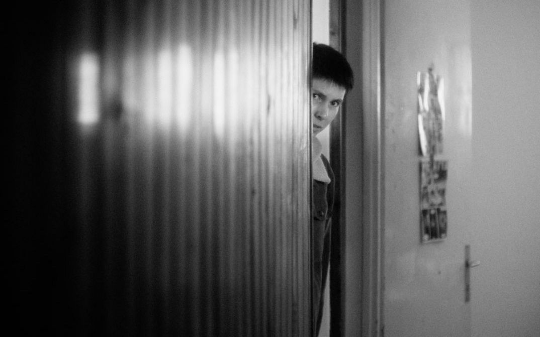 Black and white image of a person looking out of a door frame.