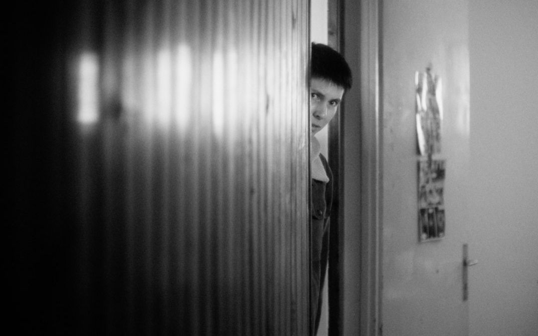 Black and white image of a person looking out of a door frame.