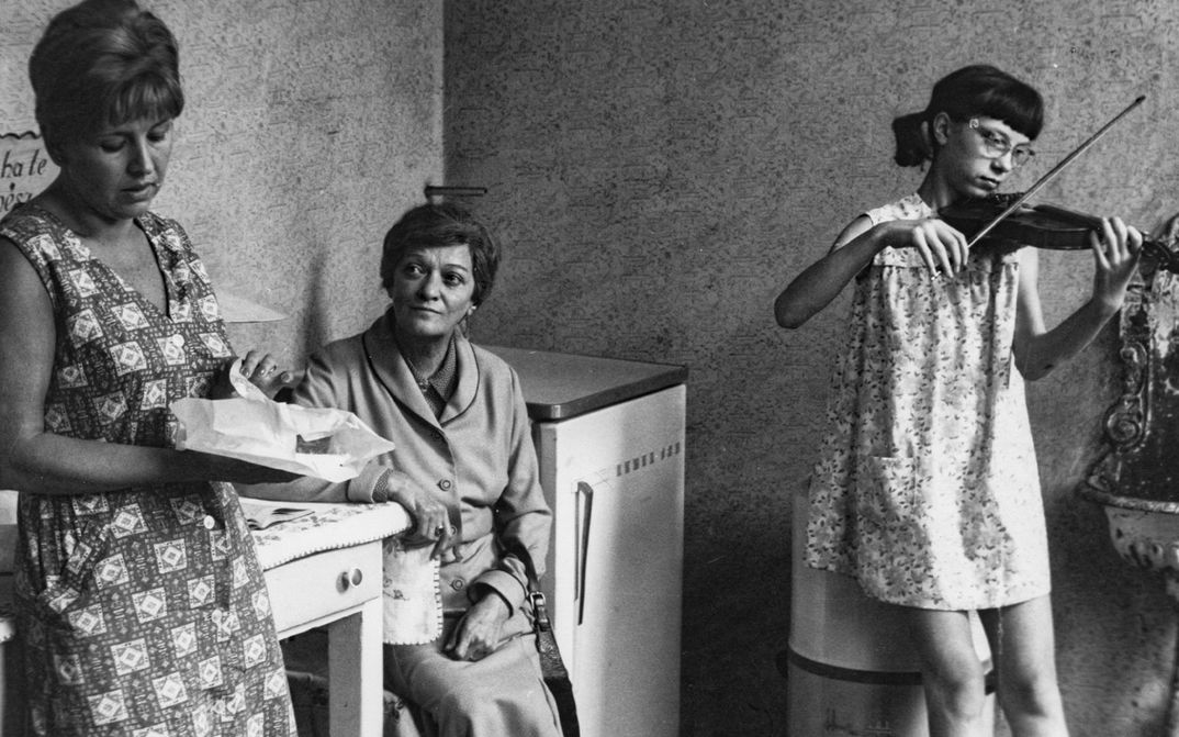 Filmstill aus The Lady from Constantinople: In einer Küche sitzen zwei Frauen und ein Mädchen spielt Geige.