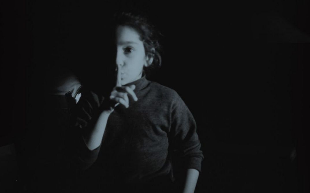 Filmstill aus MES FANTÔMES ARMENIENS von Tamara Stepanyan. Das Schwarz-weiß-Bild zeigt ein Mädchen, dass den Zeigefinger der rechten Hand vor die Lippen legt.