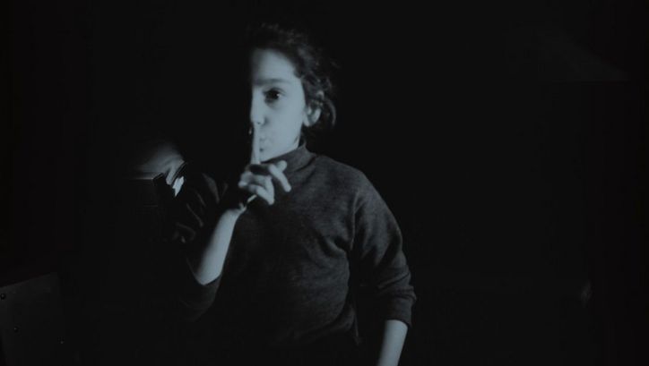Film still from MES FANTÔMES ARMENIENS by Tamara Stepanyan. The black and white image shows a girl placing the index finger of her right hand in front of her lips. 