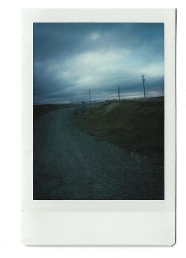 Polaroid eines dunklen Schotterwegs mit stürmischem Himmel im Hintergrund.