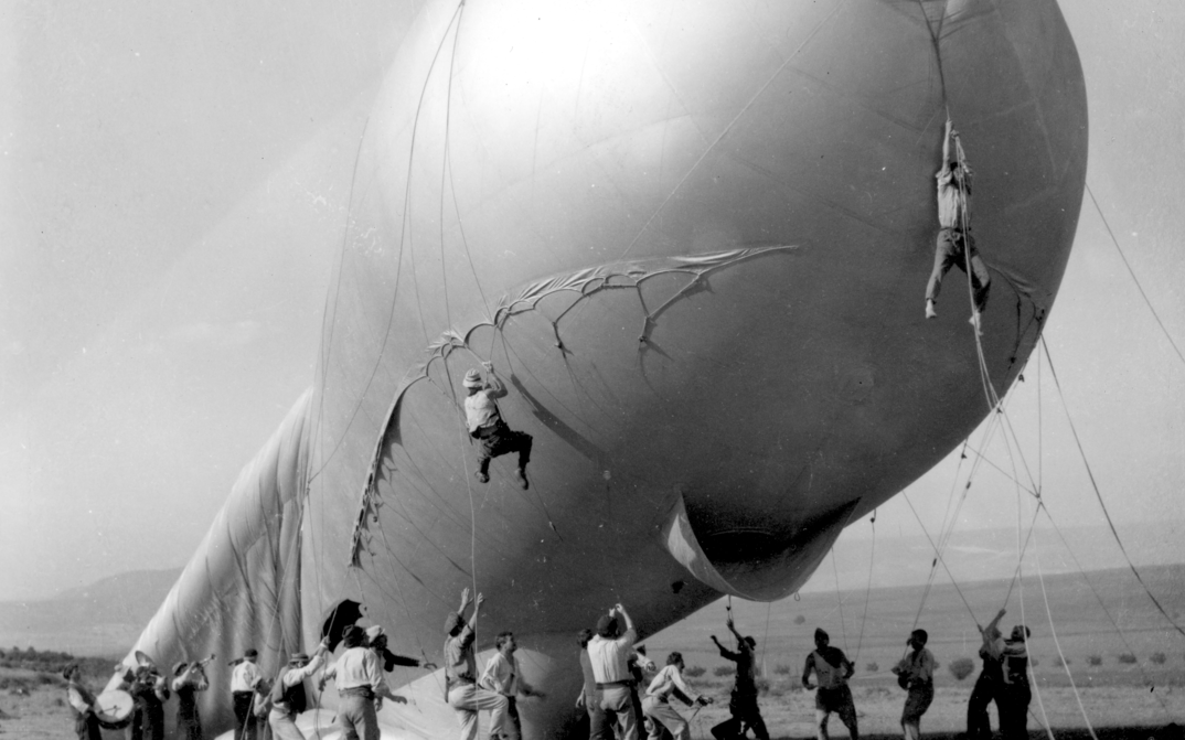 Filmstill aus THE ATTACHED BALLOON. Männer halten die Seile eines großen Sperrballons, zwei von ihnen schweben in der Luft.