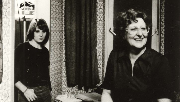 Filmstill aus VON WEGEN SCHICKSAL: Eine Frau steht lachend im Wohnzimmer, an den Türrahmen lehnt sich eine Teenagerin.