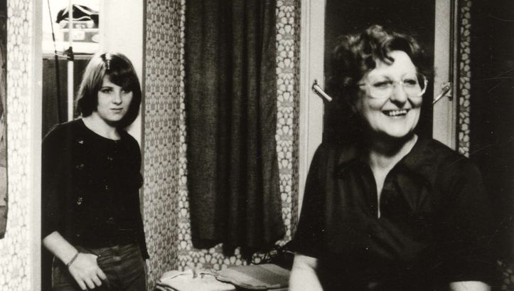 Filmstill aus VON WEGEN SCHICKSAL: Eine Frau steht lachend im Wohnzimmer, an den Türrahmen lehnt sich eine Teenagerin.