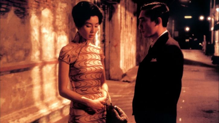 Film still from IN THE MOOD FOR LOVE: An elegantly dressed couple on the street at night. He looks at her, she looks at the ground.