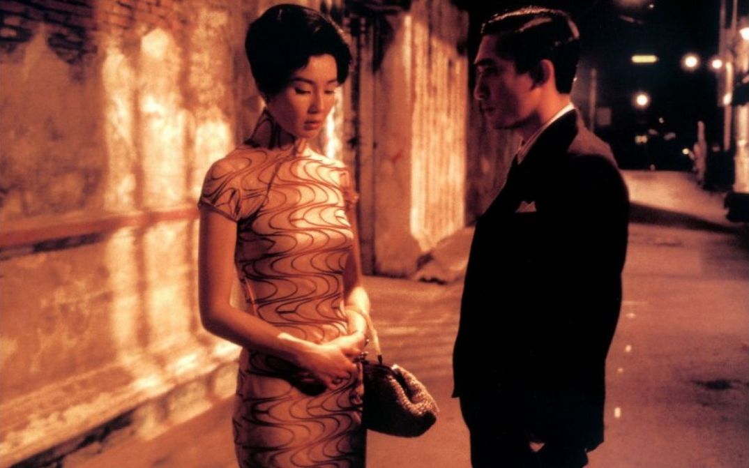 Filmstill aus IN THE MOOD FOR LOVE: Ein elegant gekleidetes Paar auf der nächtlichen Straße. Er blickt sie an, sie schaut zu Boden.