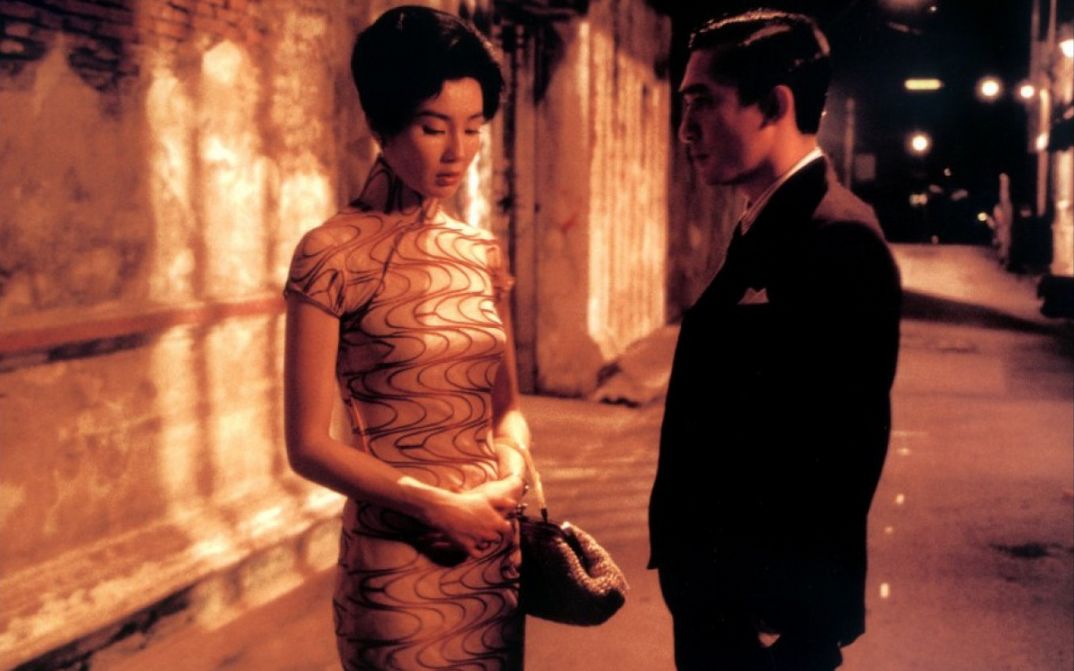 Film still from IN THE MOOD FOR LOVE: An elegantly dressed couple on the street at night. He looks at her, she looks at the ground.