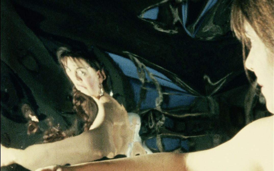 Film still from "Iris" by Maria Lassnig. It shows the side profile of a woman with her upper body exposed, looking at her reflection.