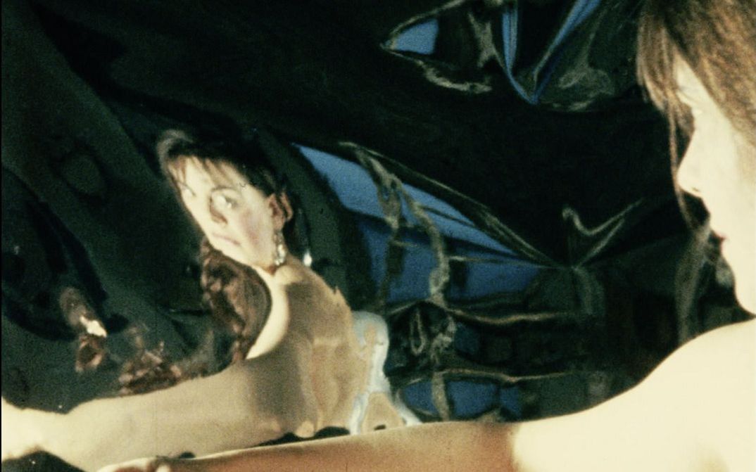 Filmstill aus "Iris" von Maria Lassnig. Zu sehen ist das Seitenprofil einer Frau mit freiem Oberkörper, die ihr Spiegelbild anschaut.