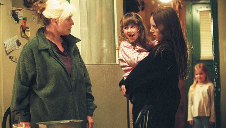Filmstill from MY LIFE WITHOUT ME: Two women are standing in a living room. One of them is holding a girl in her arms. There is another child in the background.