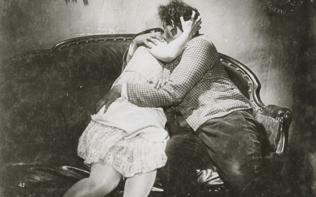 Filmstill aus SO IST DAS LEBEN: Eine Frau und ein Mann küssen und umarmen sich auf einem Sofa.