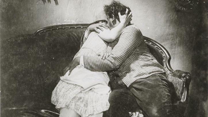 Film still from SO IST DAS LEBEN: A woman and a man kiss and embrace on a sofa.