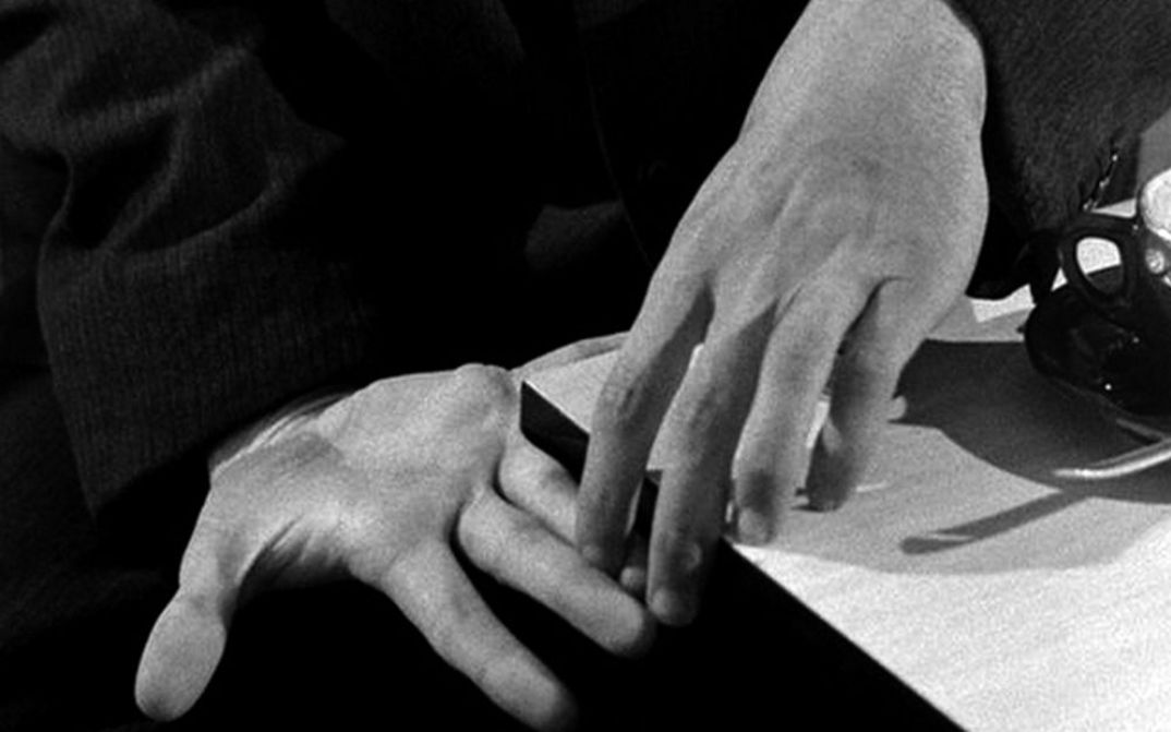 Film still from PICKPOCKET: Two hands touching with their fingertips.