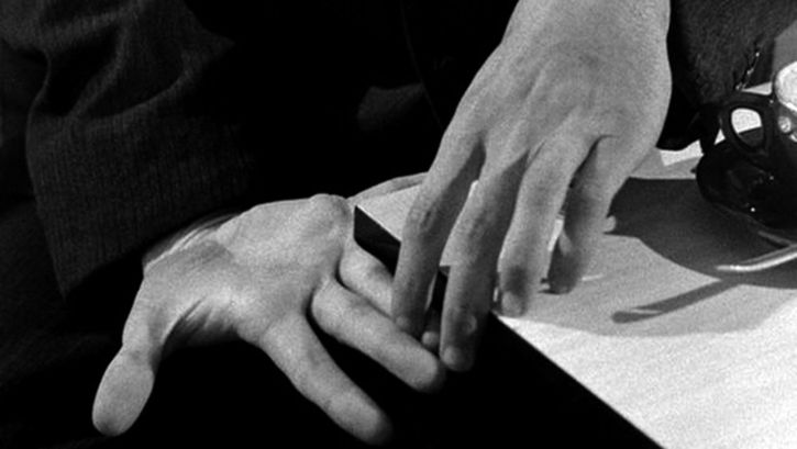 Film still from PICKPOCKET: Two hands touching with their fingertips.