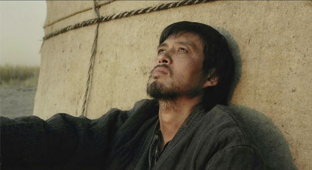 Filmstill aus „Akyn (Poet)“ von Darezhan Omirbayev. Ein Mann sitzt an einer Jurte und schaut nachdenklich nach oben. 