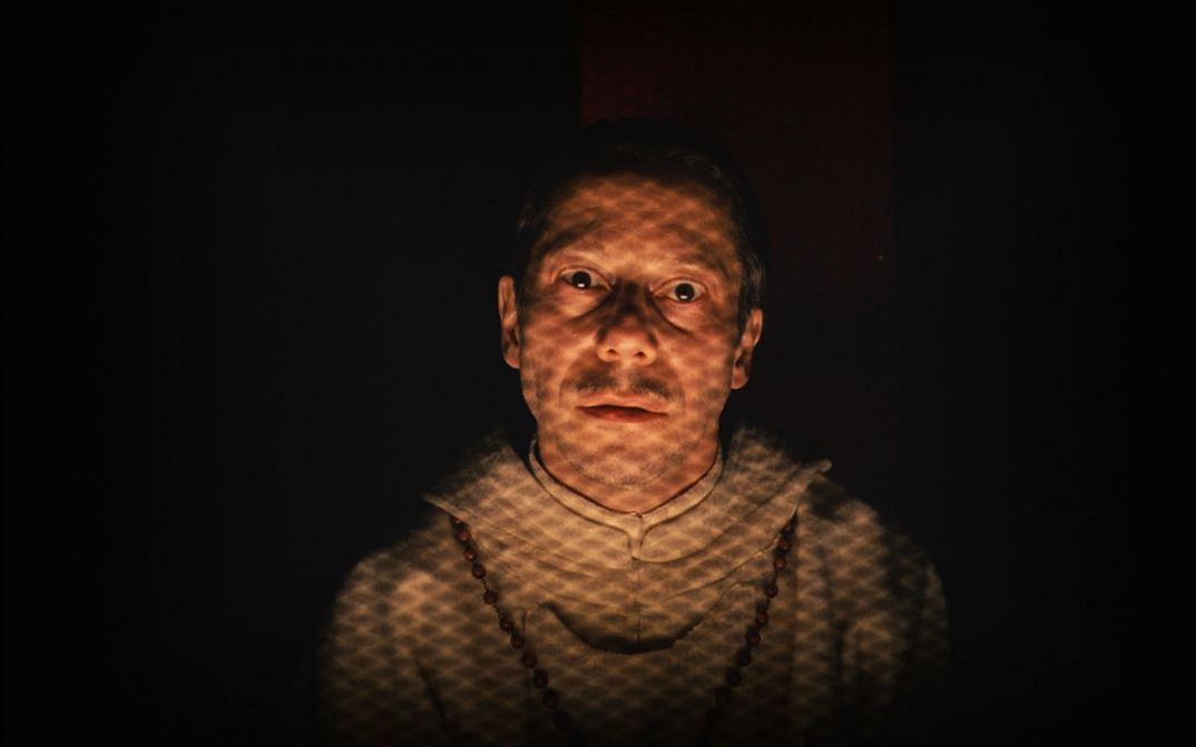 Film still from THE GRAND BUDAPEST HOTEL. Mathieu Amalric as the priest looks head-on into the camera.