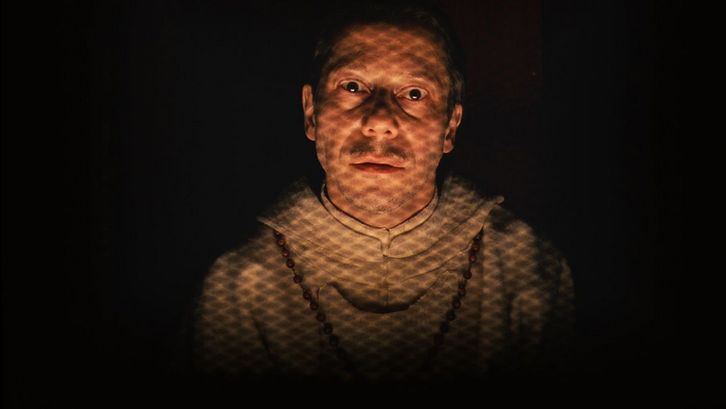 Filmstill aus THE GRAND BUDAPEST HOTEL. Mathieu Amalric als Priester blickt frontal in die Kamera.