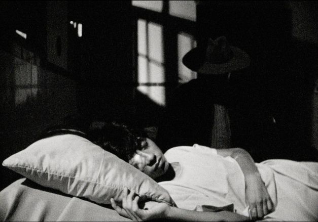 Film still from PUNKU by J.D. Fernández Molero. The black and white image shows a close-up of a sleeping person on a bed.