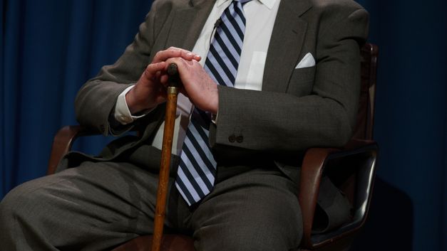 Still from the film "Black Beauty: For a Shamanic Cinema" by Grace Ndiritu. A man in a suit sits in an armchair and rests his hands on a cane.