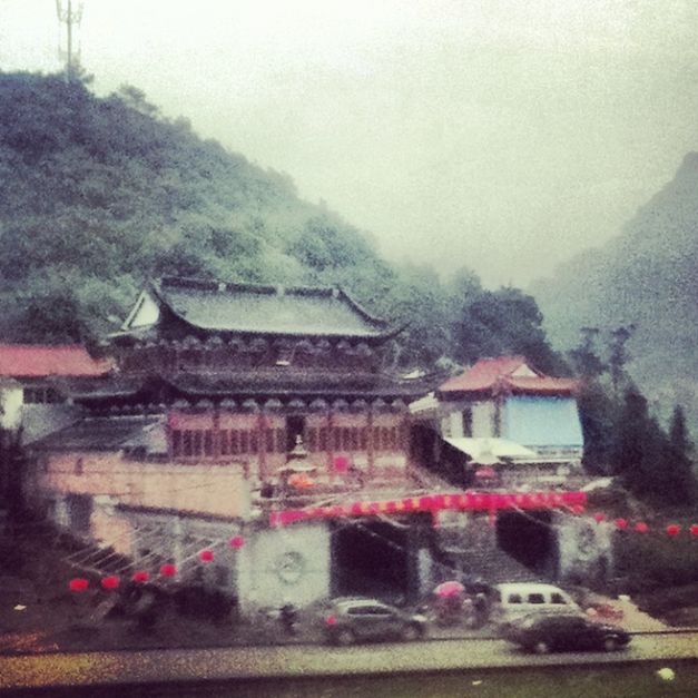 A hazy image of a traditional Chinese building set against green mountains.
