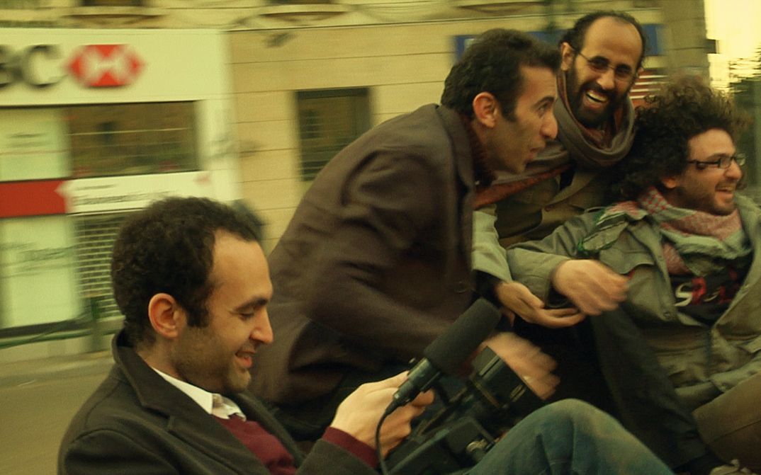 Film still from IN THE LAST DAYS OF THE CITY: Four men laughing with a camera on the street. The background is blurred.