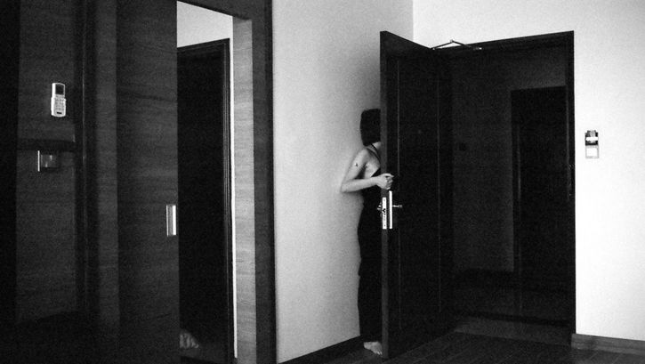 Still from the film "Jet Lag" by Zheng Lu Xinyuan. A black-and-white image of a girl hiding behind an open hotel room door, with the side of her body and her hair visible.