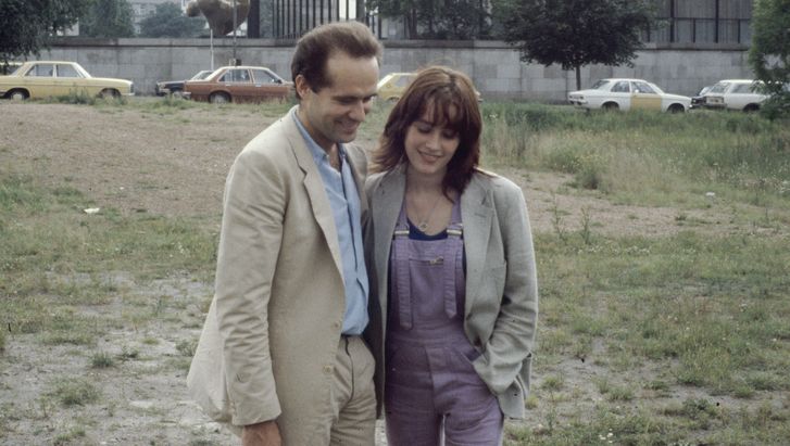 Film still from BERLIN CHAMISSOPLATZ: A man and a woman stand close together on a wasteland in front of the Neue Nationalgalerie in Berlin.